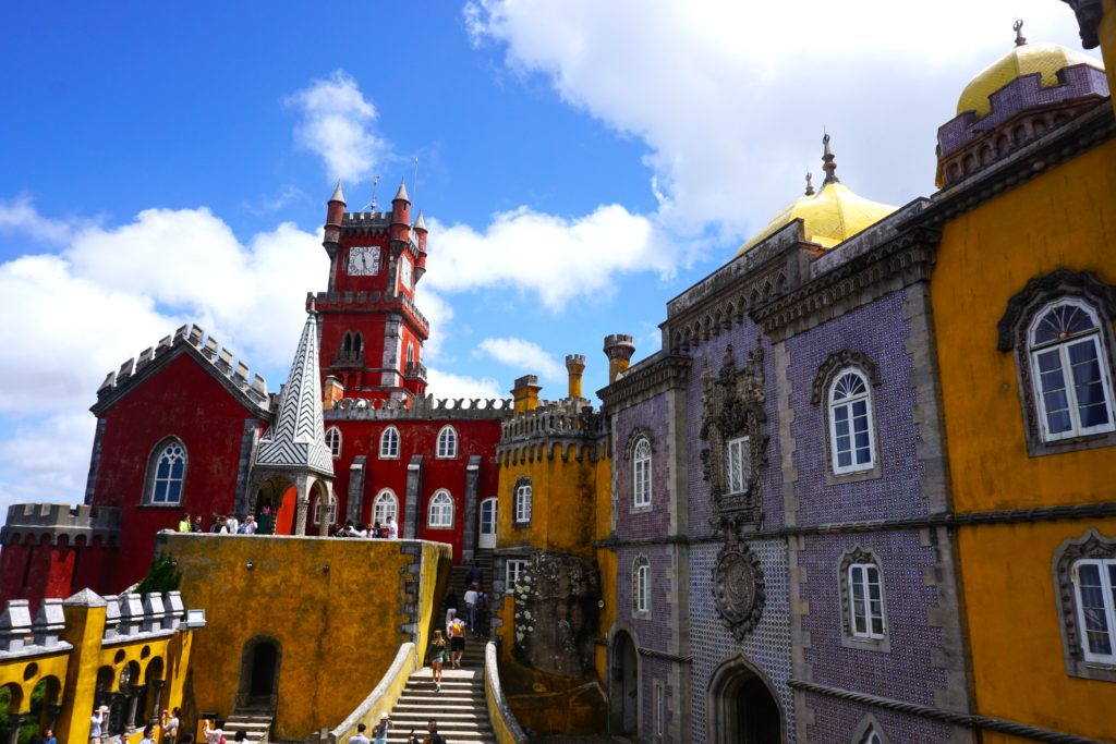 The colorful Pena Palace in Sintra, near Lisbon, with its vivid red and yellow walls, ornate tilework, and mythical statues, stands as a striking example of Romanticist architecture, an essential day trip from Lisbon.