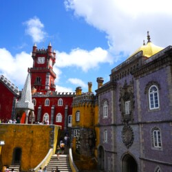The colorful Pena Palace in Sintra, near Lisbon, with its vivid red and yellow walls, ornate tilework, and mythical statues, stands as a striking example of Romanticist architecture, an essential day trip from Lisbon.