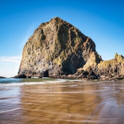 Haystack Rock towers above the sandy shores of Cannon Beach, a scenic and iconic day trip destination just a drive away from Portland, Oregon.