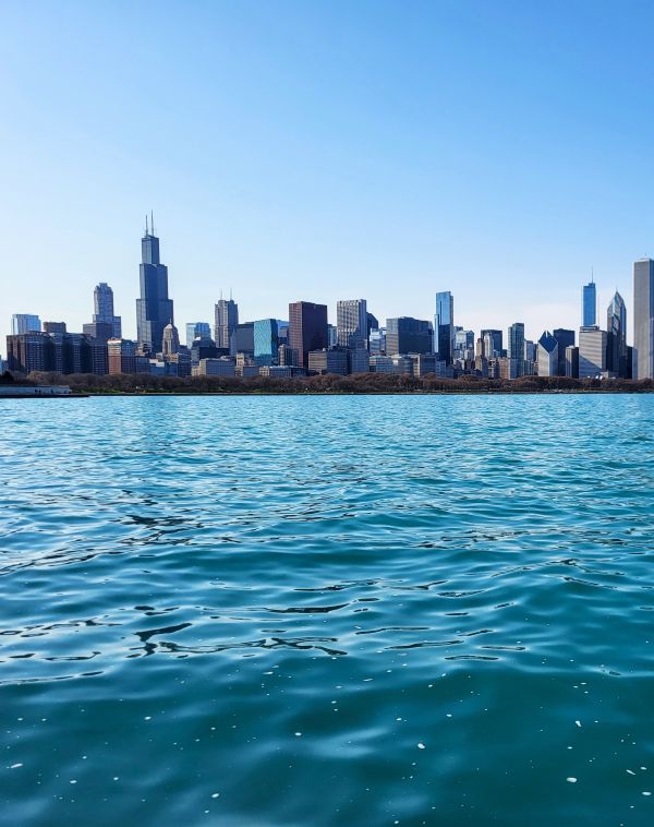 Chicago's skyline stands majestic against a clear sky, viewed from the tranquil waters near Museum Campus, a perfect sightseeing spot for a girls weekend in Chicago.