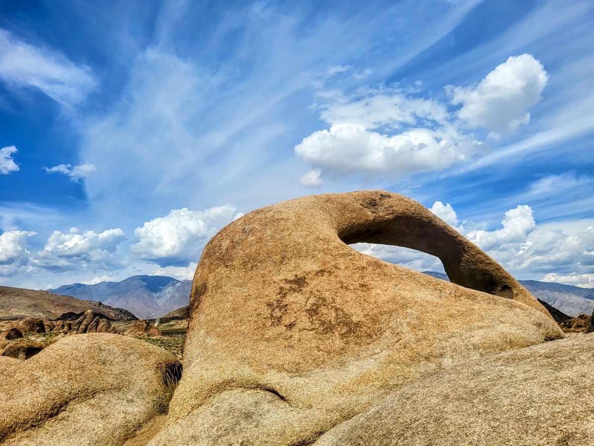 Spectacular view of a distinctive arch-shaped rock against a vivid blue sky with wispy clouds, captured while hiking in the Alabama Hills.