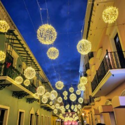 Illuminated spherical light installations hanging above a street in Old San Juan, Puerto Rico, creating a magical atmosphere against the twilight sky, a must-see during Christmas in San Juan.