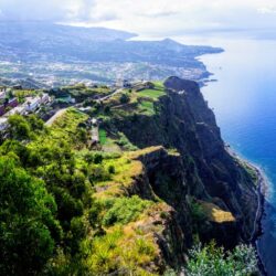 View from Cabo Girão in Madeira, showcasing terraced fields and a village on a cliff's edge. The azure Atlantic Ocean stretches to the horizon, highlighting stops on a Madeira itinerary.