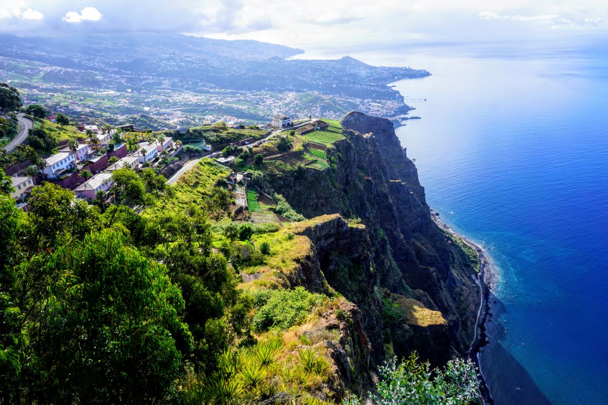 View from Cabo Girão in Madeira, showcasing terraced fields and a village on a cliff's edge. The azure Atlantic Ocean stretches to the horizon, highlighting stops on a Madeira itinerary.