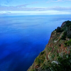Cliffside view of the tranquil Atlantic Ocean from Madeira's north coast with a clear sky above and lush greenery on the slope. Perfect for a serene day on a Madeira itinerary.