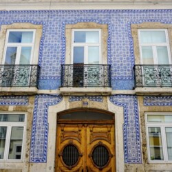The facade of a Lisbon building adorned with traditional Portuguese blue azulejo ceramic tiles, with ornate wrought-iron balconies, capturing the essence of Lisbon's architectural beauty for a detailed Lisbon itinerary.