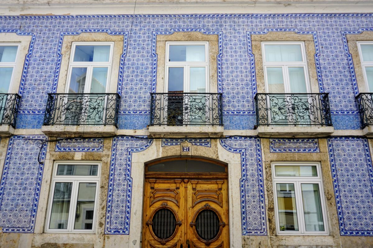The facade of a Lisbon building adorned with traditional Portuguese blue azulejo ceramic tiles, with ornate wrought-iron balconies, capturing the essence of Lisbon's architectural beauty for a detailed Lisbon itinerary.