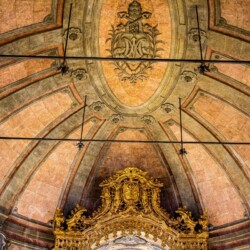 Intricate ceiling details of Clérigos Church in Porto, featuring ornate stonework and a lavish golden altar, embodying the rich baroque architecture that visitors can admire as part of their Porto travel itinerary.