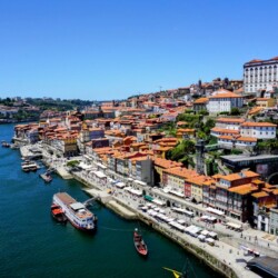 Aerial view of the Douro River in Porto, with traditional Rabelo boats floating by the Ribeira District's colorful terraced buildings, a vibrant and picturesque scene for those enjoying a Porto itinerary.