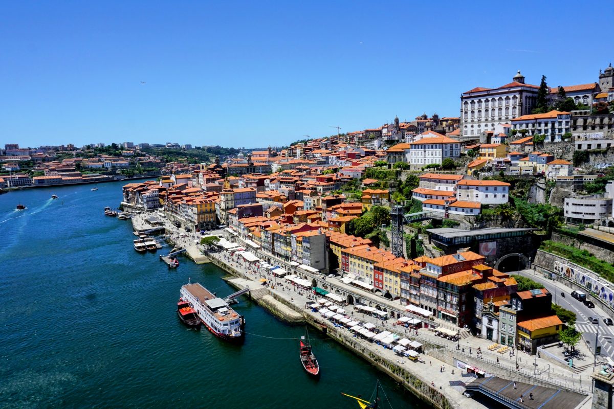 Aerial view of the Douro River in Porto, with traditional Rabelo boats floating by the Ribeira District's colorful terraced buildings, a vibrant and picturesque scene for those enjoying a Porto itinerary.