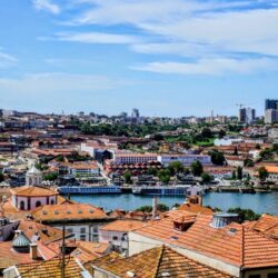 Overlooking the city of Porto, the view from Mirador da Vitória includes terracotta rooftops, the Douro River, and distant modern skyscrapers under a vast blue sky, capturing the city's blend of historic charm and urban development.