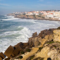 Praia das Maçãs in Sintra, with its rugged cliffs and foamy waves. This scenic Sintra beach is nestled against a backdrop of a quaint seaside village.