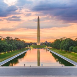 Sunrise at the National Mall with the Washington Monument reflected in the Reflecting Pool. Green trees and a colorful sky complete the tranquil scene on a DC itinerary.
