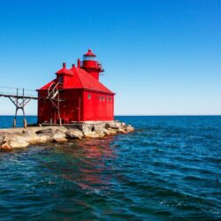 The vibrant red Sturgeon Bay Canal North Pierhead Lighthouse in Door County, a maritime beacon for Midwest getaways, stands out against the blue sky and lake.