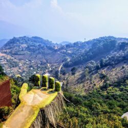 Sweeping view of the verdant valleys near Hobbitenango, Guatemala, with a whimsical oversized hand sculpture protruding from a cliff, epitomizing the unique attractions to discover on a Hobbitenango day trip.