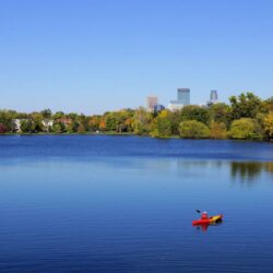 A kayaker enjoying a sunny day on a calm lake with Minneapolis's urban skyline in the distance, a Midwest summer vacation highlight.