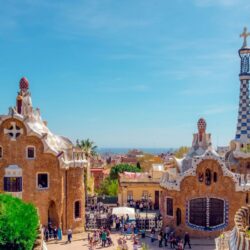 The iconic gingerbread house-like pavilions at the entrance of Park Güell, with tourists milling about, are an essential experience for any Barcelona itinerary.