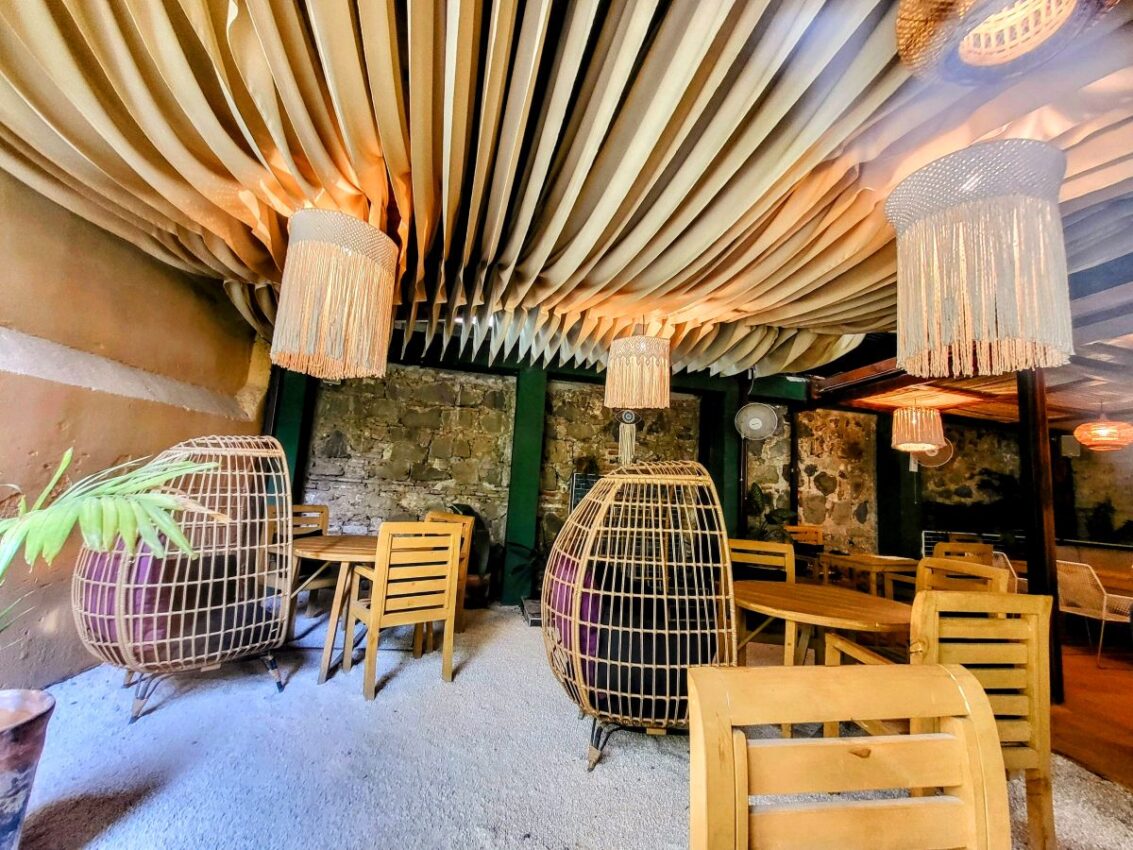 Chic and unique interior of a restaurant in Antigua, featuring avant-garde wicker pod chairs and draped ceiling design, creating an inviting atmosphere for diners.