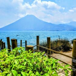 A rustic wooden fence borders a pebbled path in San Marcos, leading to the serene shores of Lake Atitlan, inviting exploration and tranquility.