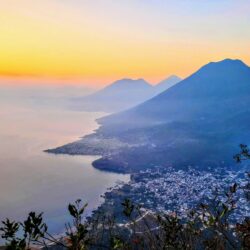 The golden hour casts a soft glow over the volcanoes bordering Lake Atitlan, viewed from a high vantage point in San Marcos, capturing a moment of serene beauty.