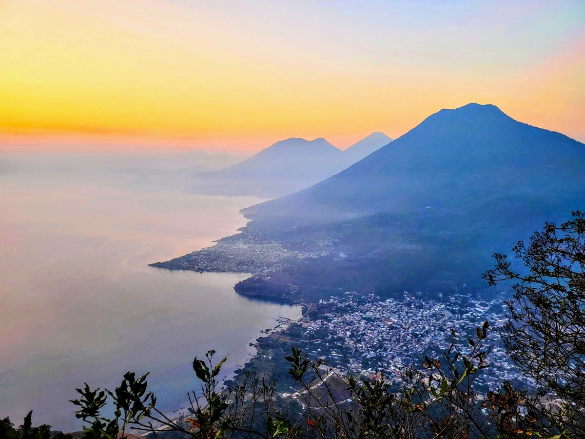 The golden hour casts a soft glow over the volcanoes bordering Lake Atitlan, viewed from a high vantage point in San Marcos, capturing a moment of serene beauty.